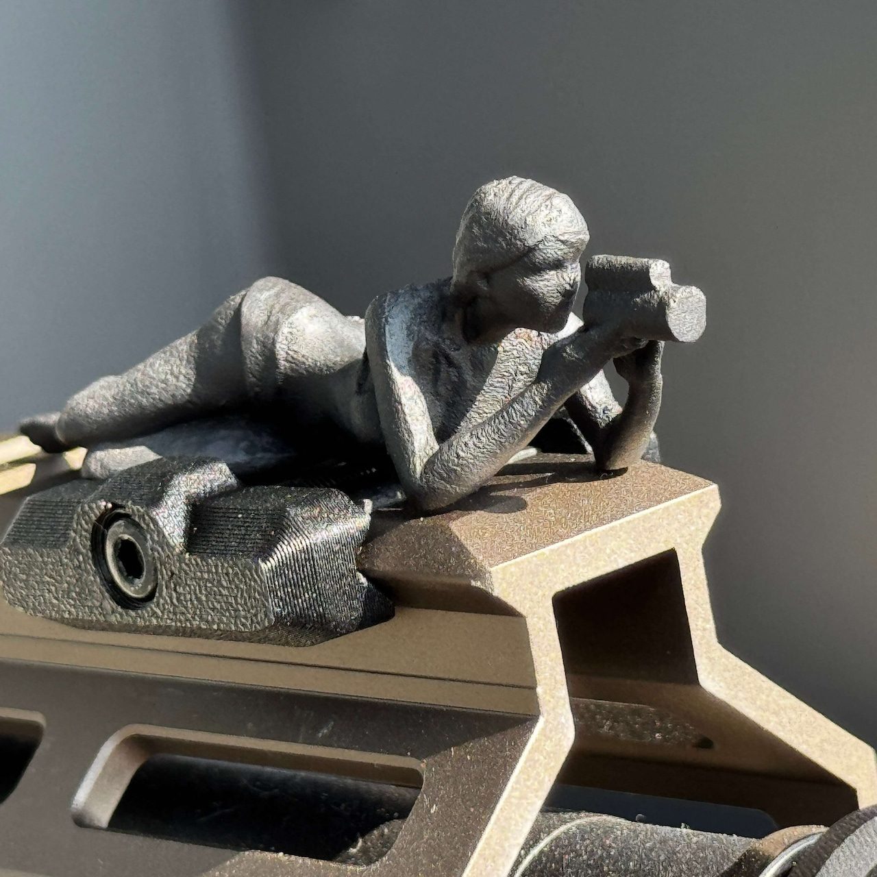 Spotter G figure lying prone with a scope, sunlit steel detail